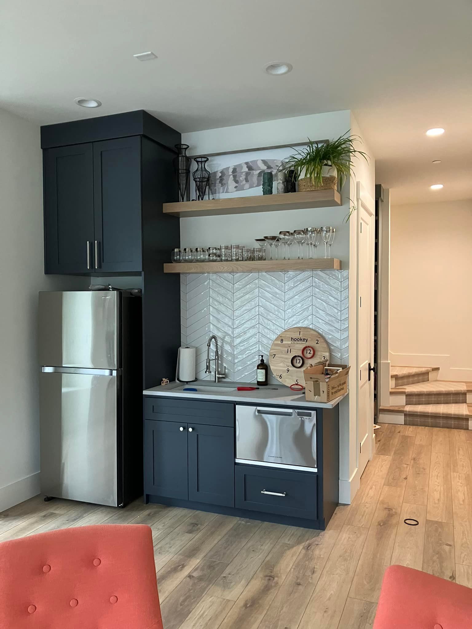 A kitchen wet bar with navy cabinets, stainless steel appliances, wood shelves, and a decorative tile backsplash.
