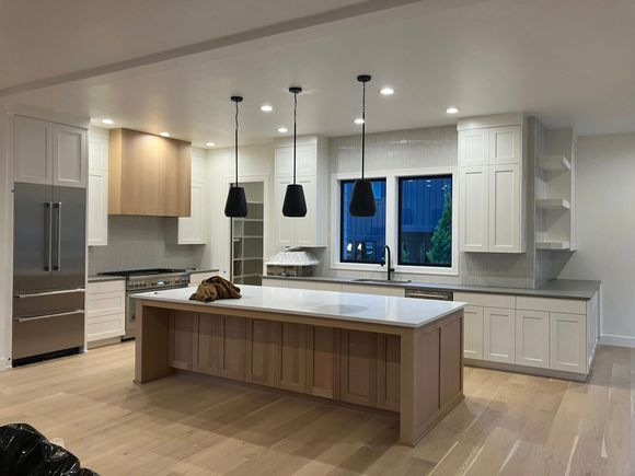 A modern kitchen features a large wooden island with a marble countertop, white cabinetry, and three pendant lights.