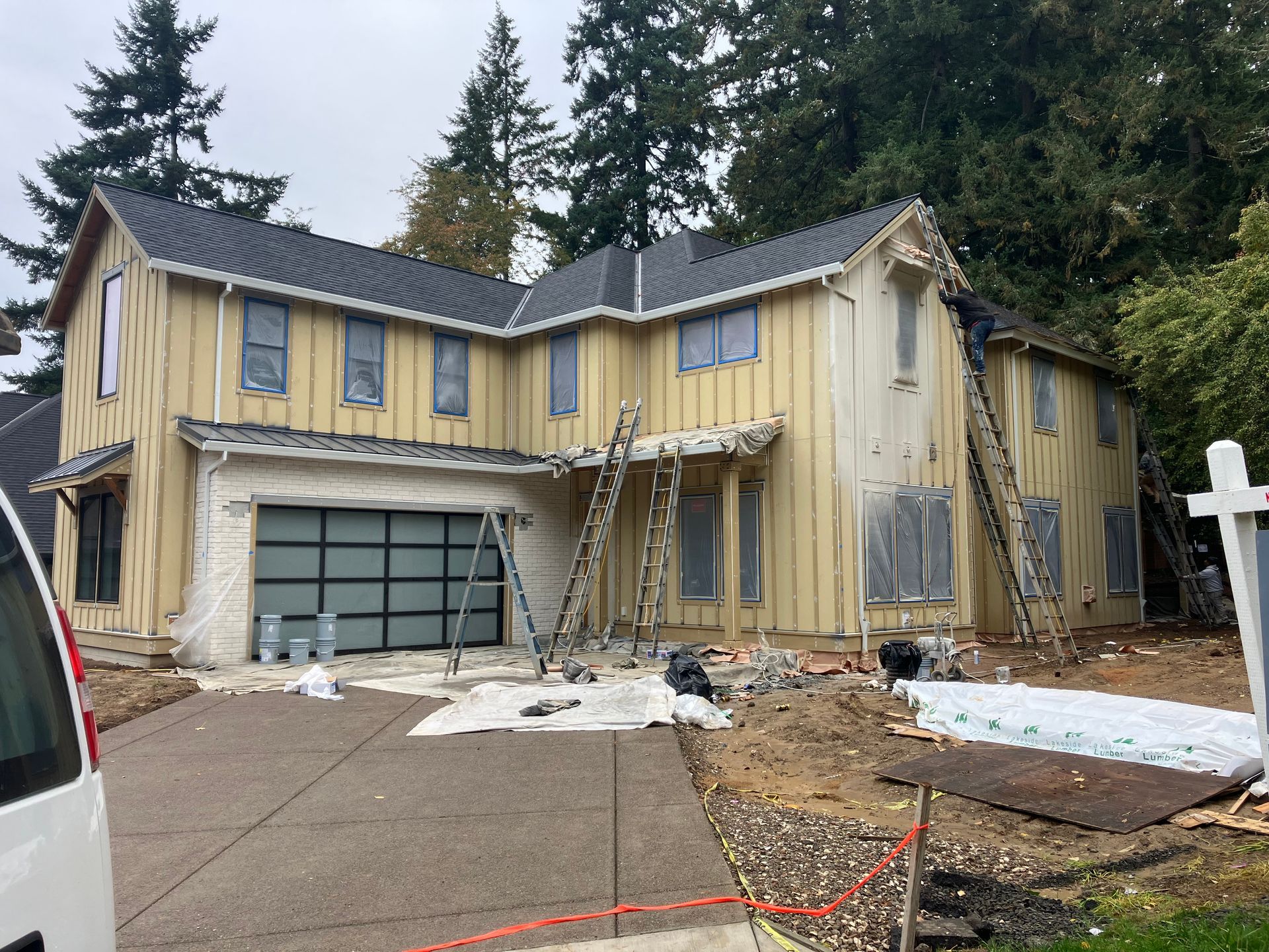 Damaged two-story yellow house with broken windows, tarp on roof, and debris in driveway after a storm