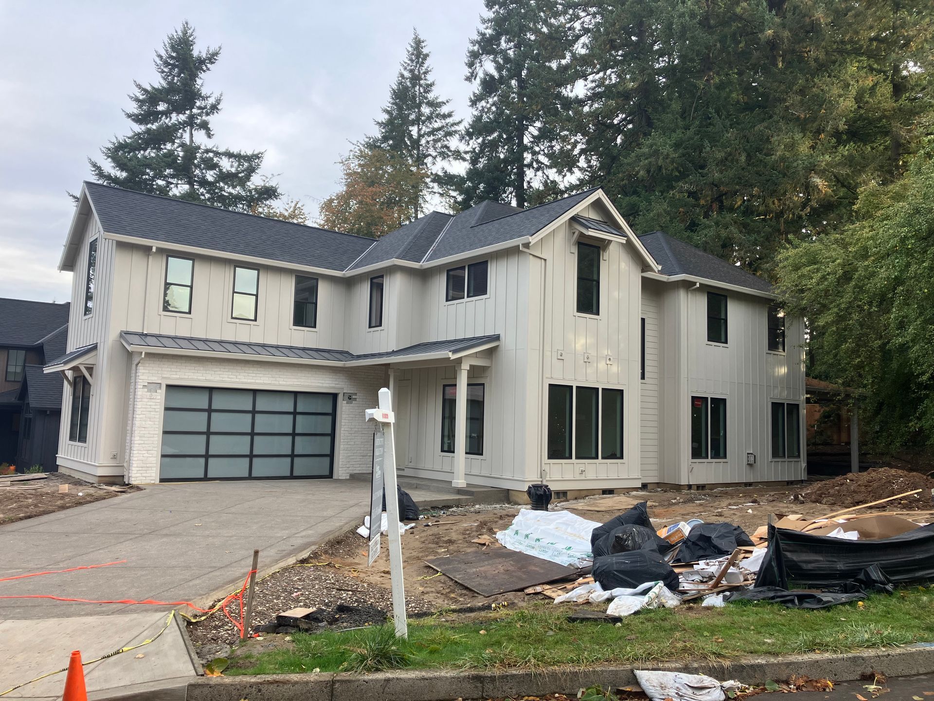 Two-story beige house with attached garage, front yard under construction, and trees in the background