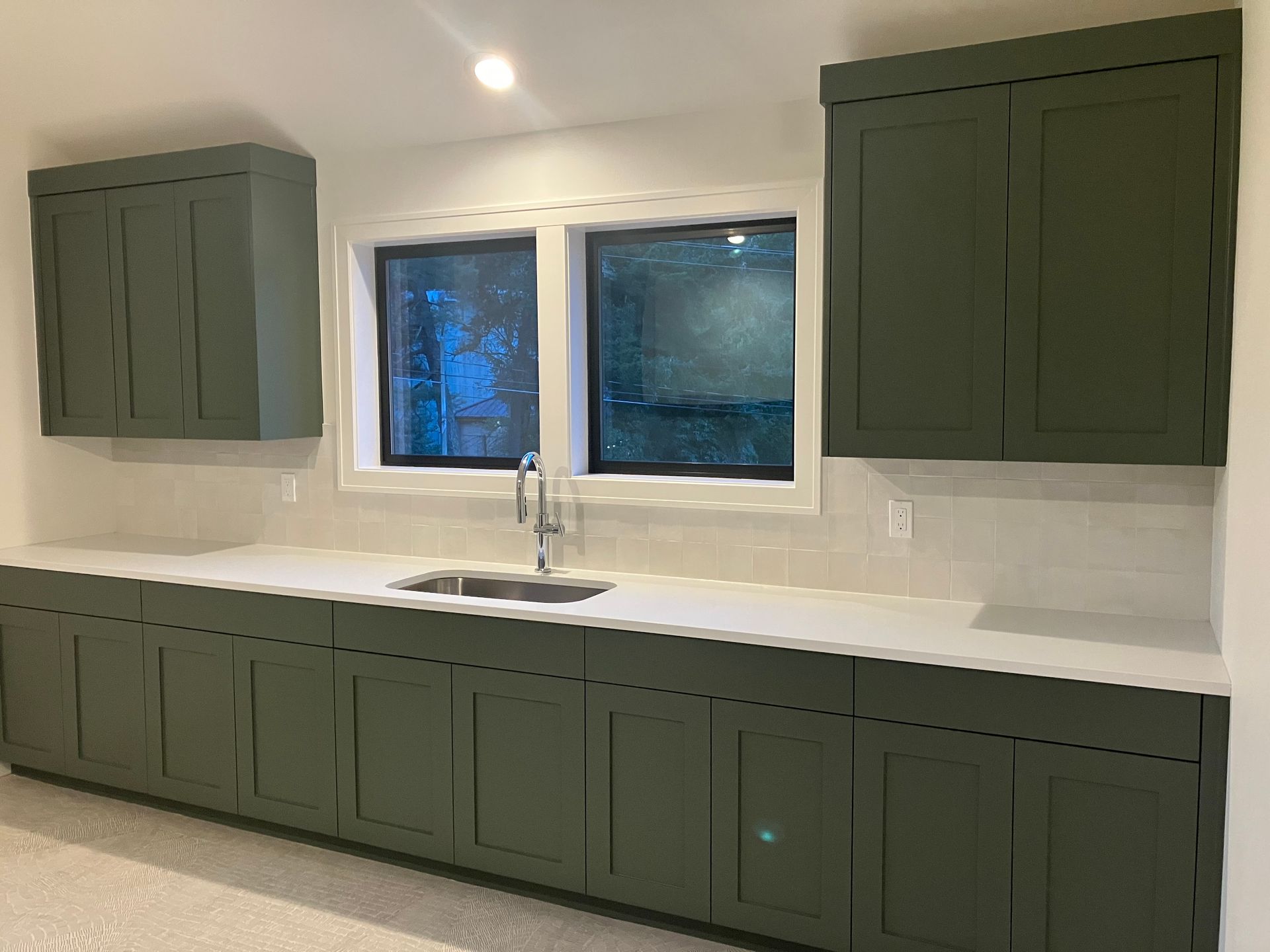 Modern kitchen with olive-green cabinets, white countertops, and a centered window over the sink