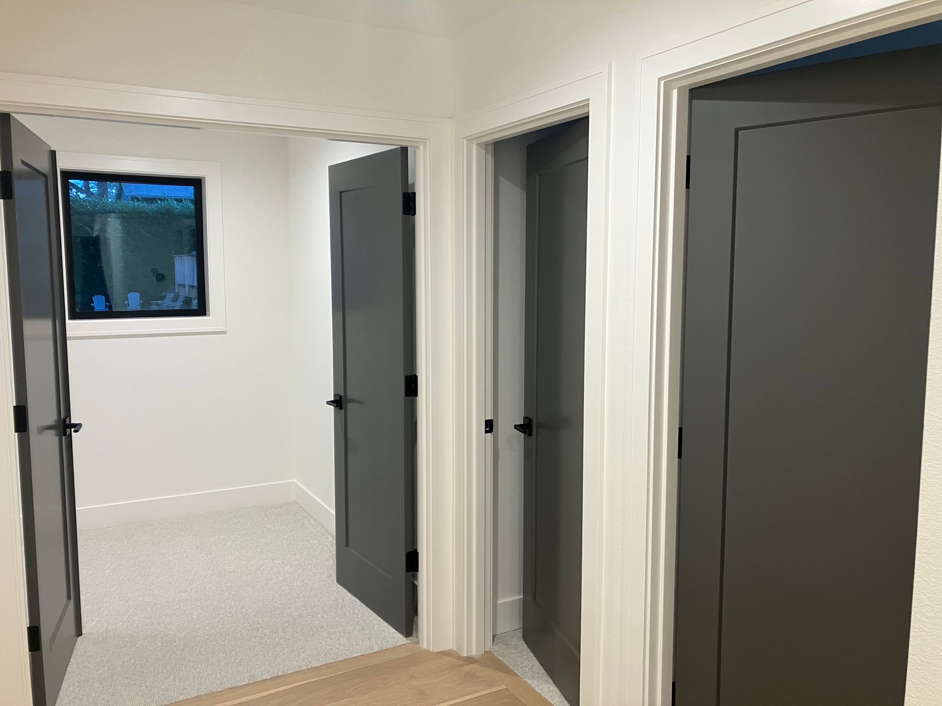 Bright hallway with white walls, gray doors, and a small window at the end.