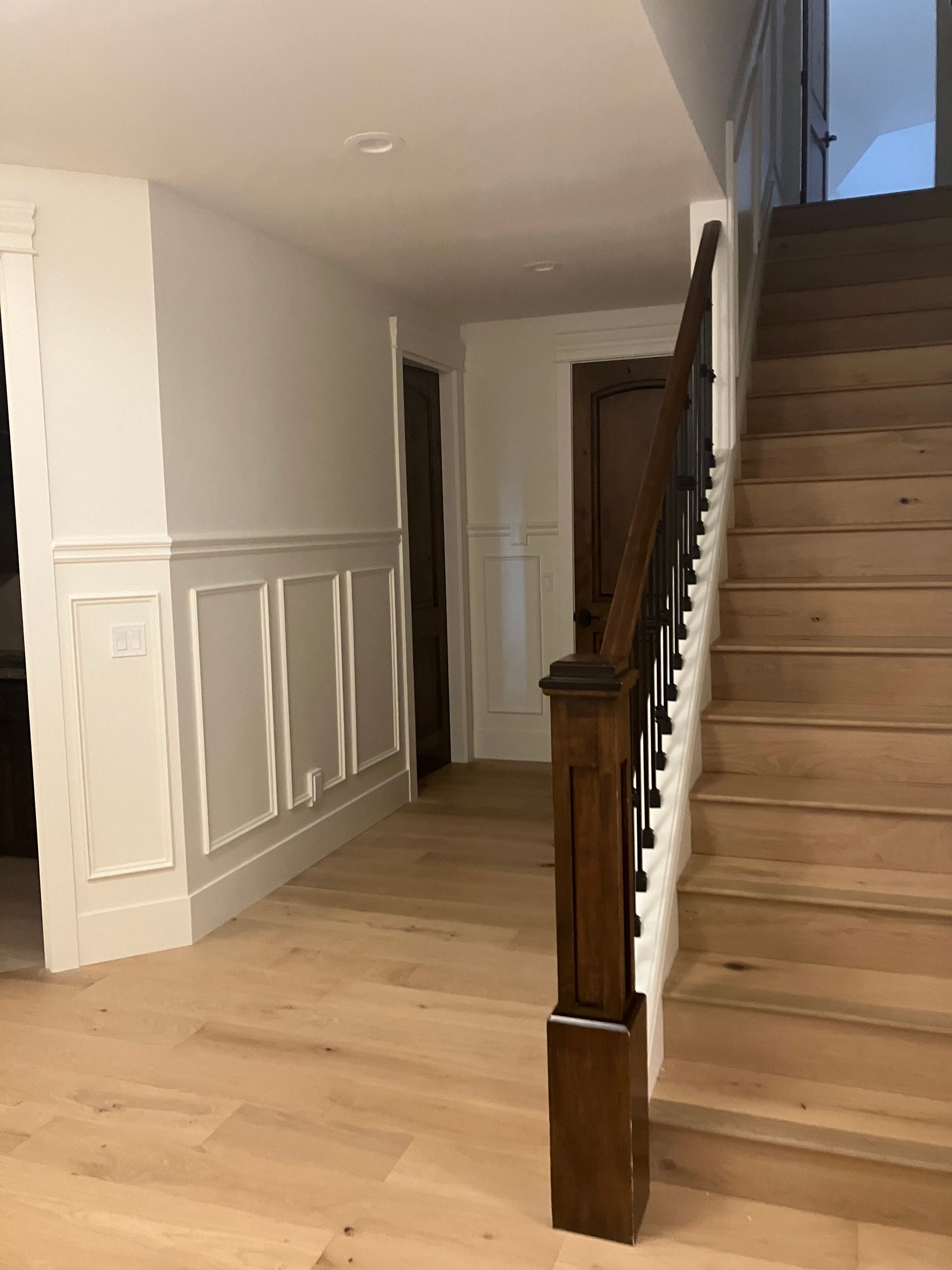 Interior hallway with wooden staircase, white paneled walls, and light wood flooring