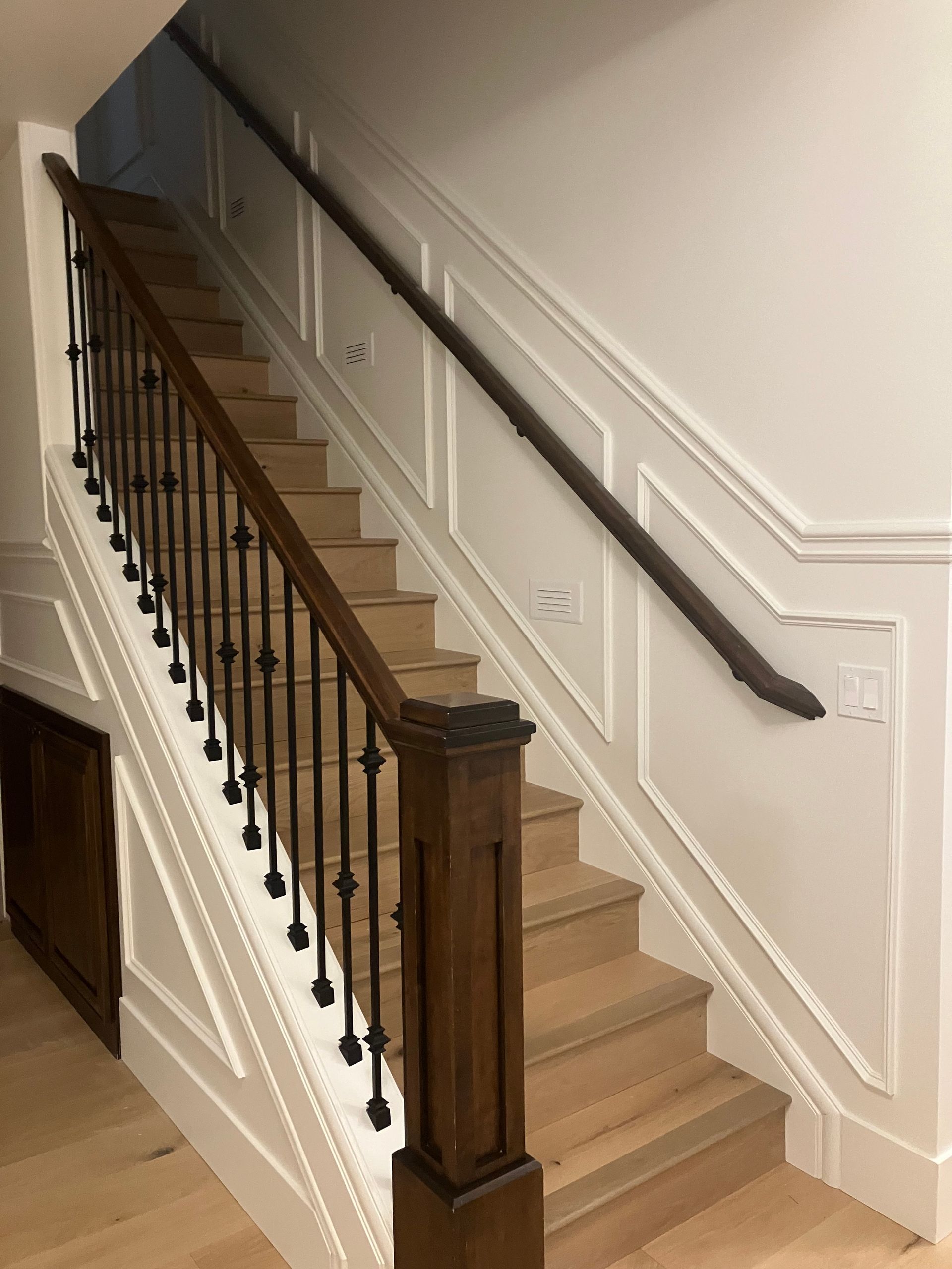 Indoor staircase with beige carpet, dark wooden banister, and white paneled walls