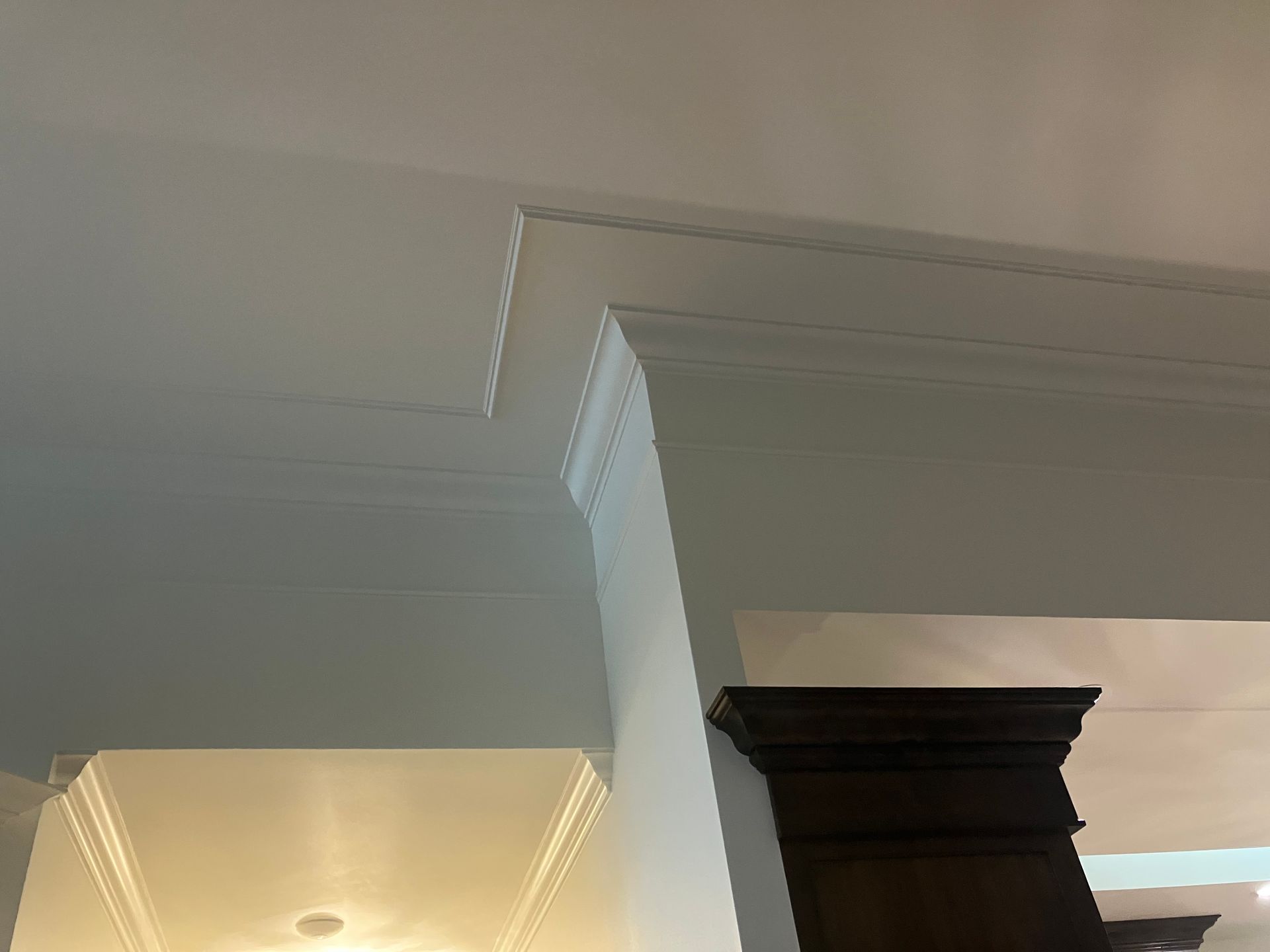 Interior ceiling with decorative crown molding and a dark wood column, lit by warm recessed lights.