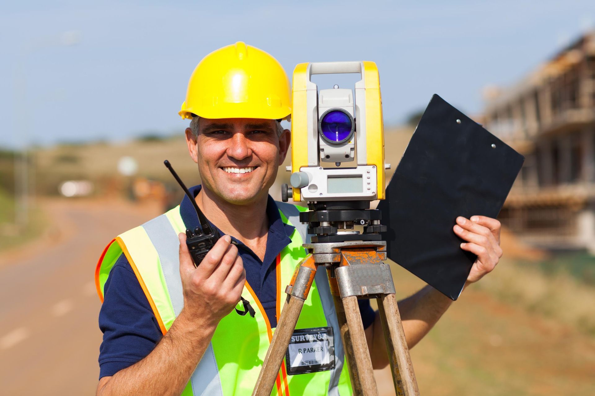 Surveyor in yellow hard hat smiles, holding radio.