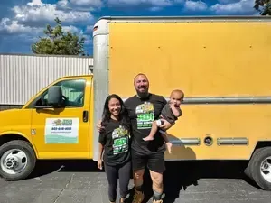 A man and woman are holding a baby in front of a yellow truck.