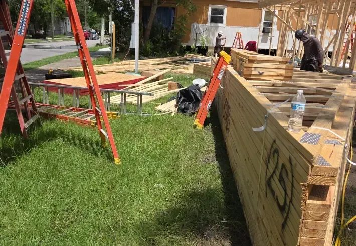 People assembling a large wooden structure outdoors on a grassy lawn with ladders and tools
