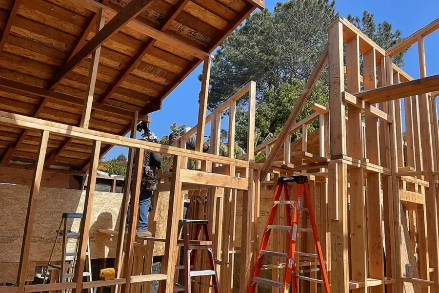 Wood-framed house under construction with red ladder and exposed rafters outdoors