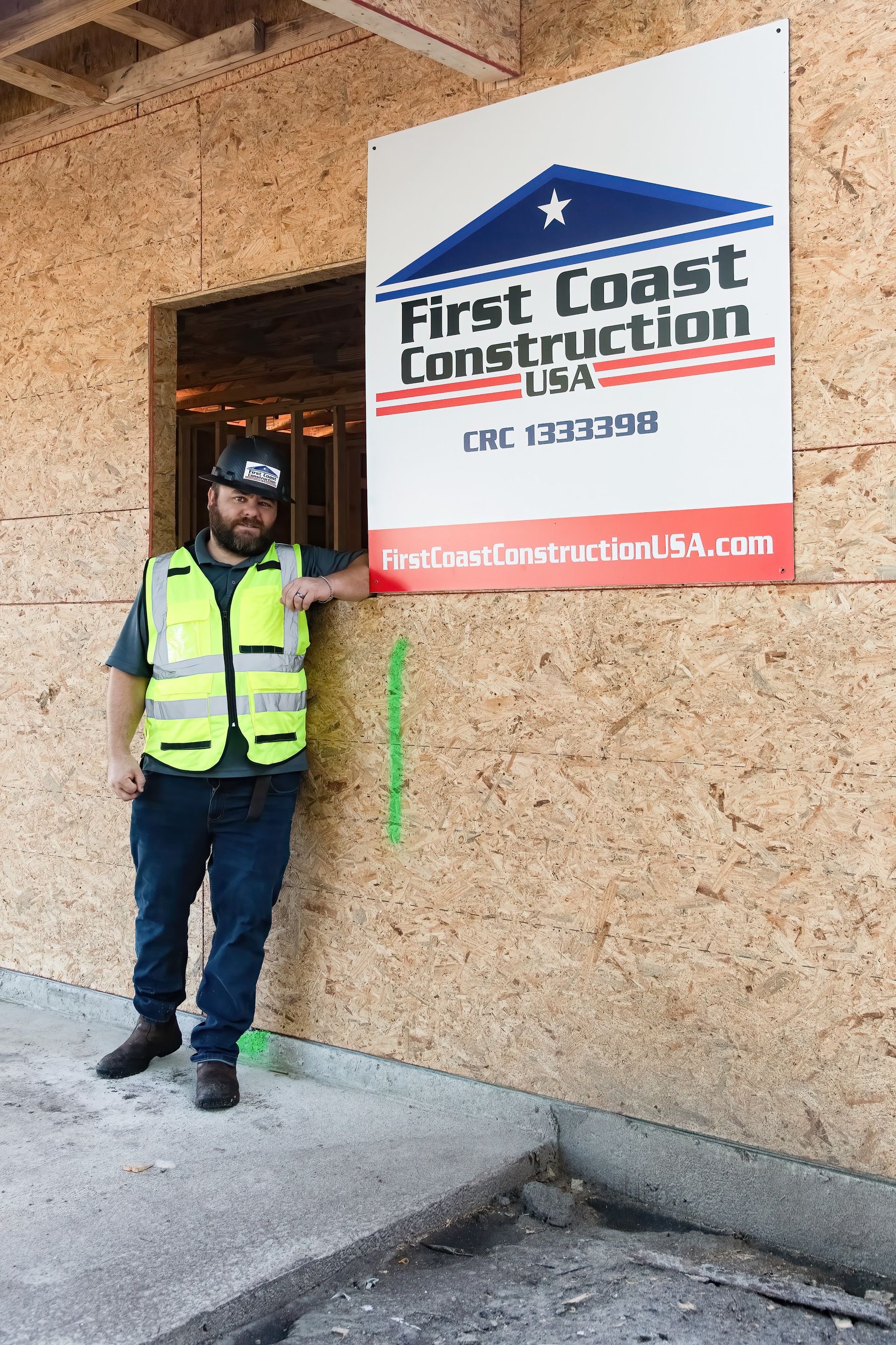 Worker in neon safety vest standing by a First Coast Construction sign outside a building.