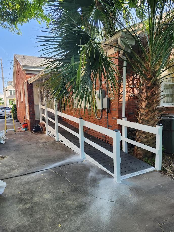 White ramp railing beside a brick house walkway with palm trees and concrete driveway