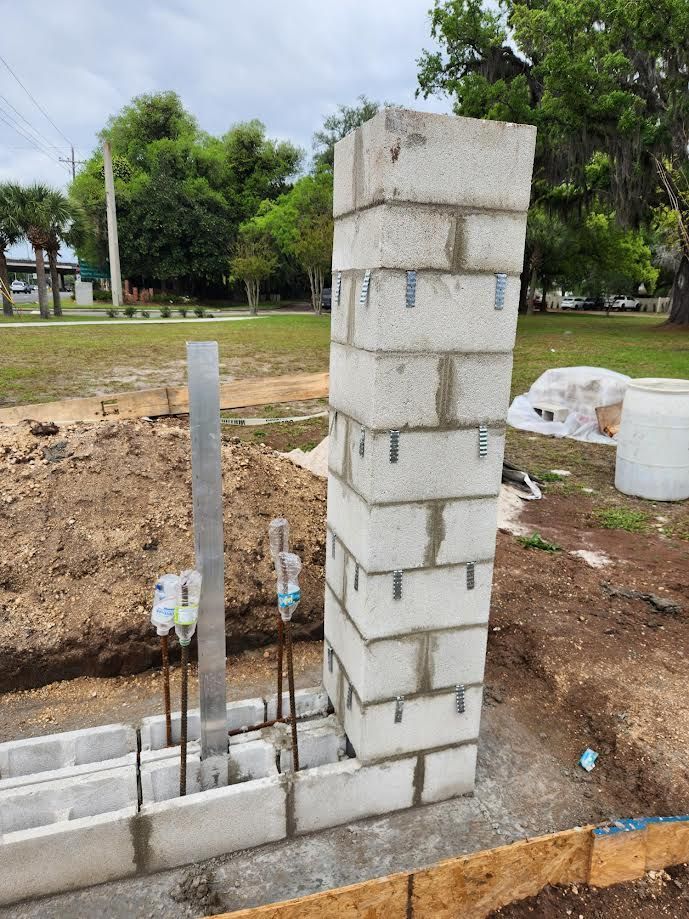 Partially built brick pillar beside a low wall, with rebar and concrete in a park setting