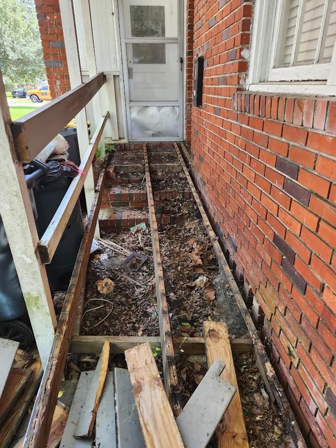 Narrow brick side yard under construction, with exposed dirt, wooden framing, and a white door at the end.