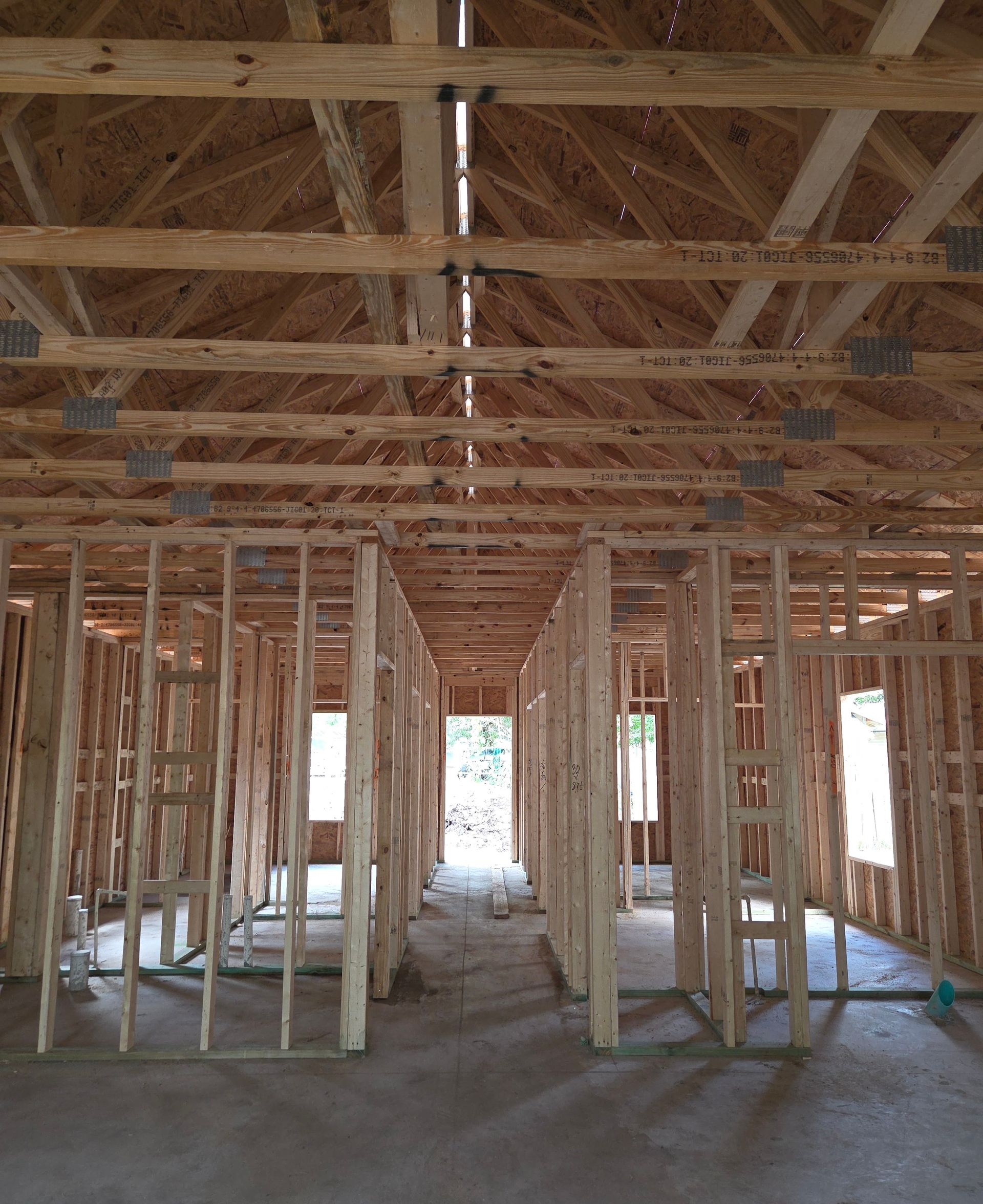 Interior of a house under construction, showing exposed wooden framing and a concrete floor.