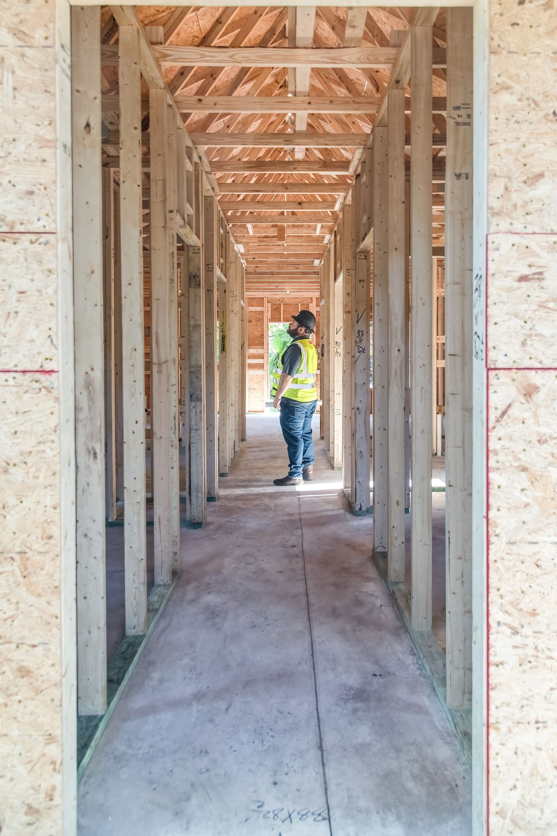 Worker in a framed hallway at a construction site, wearing a yellow safety vest and hard hat.