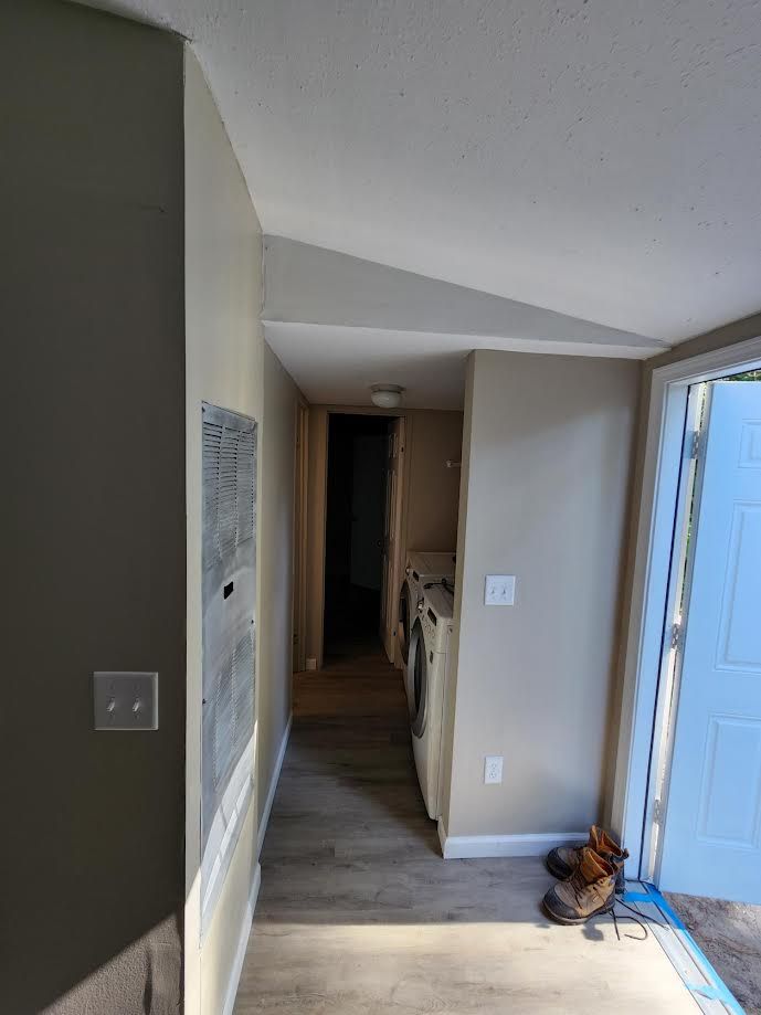 Narrow hallway with gray walls, wood floor, and an open front door showing bright blue outside.