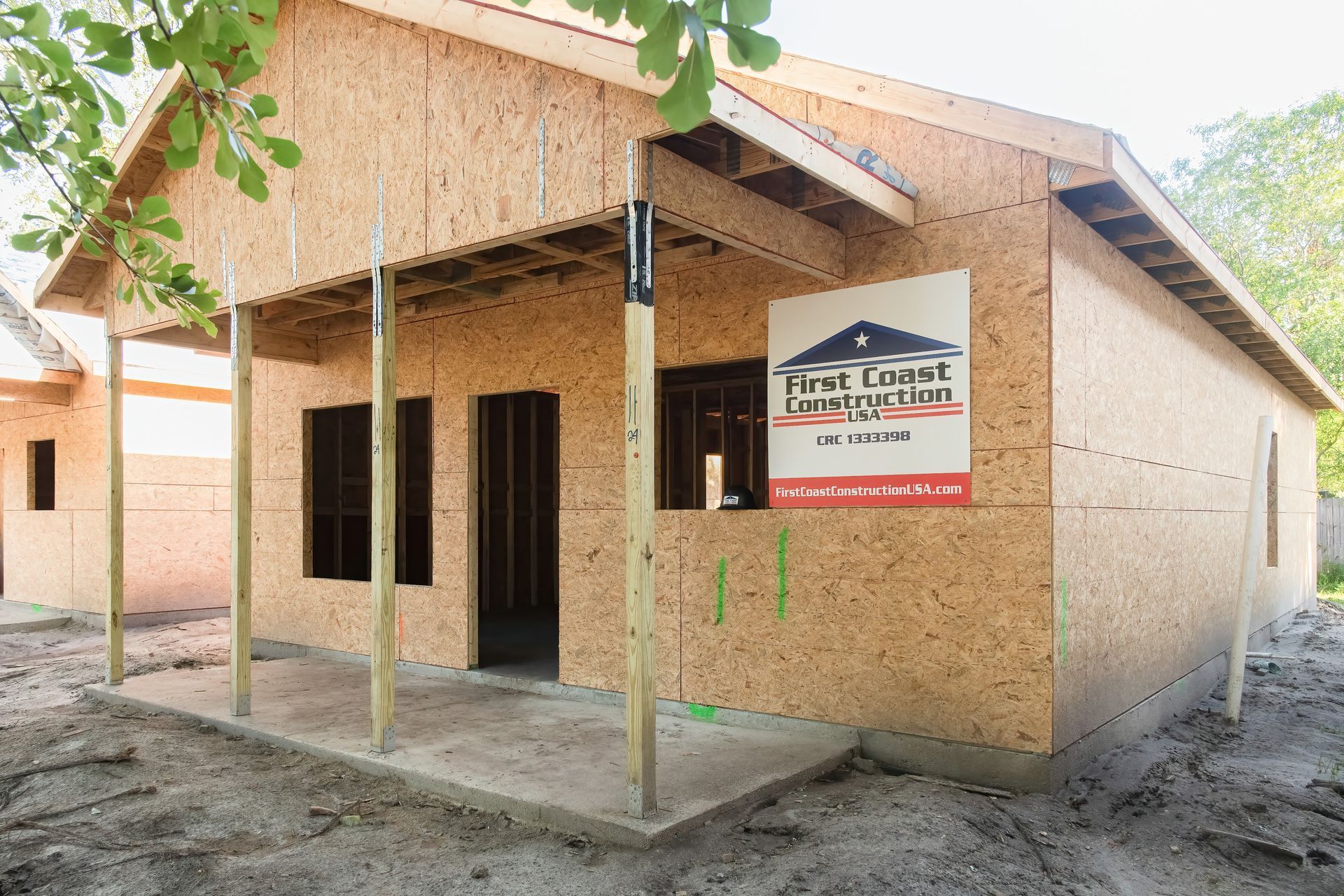 Small unfinished house with a porch and signboard, shown in a sandy outdoor setting.