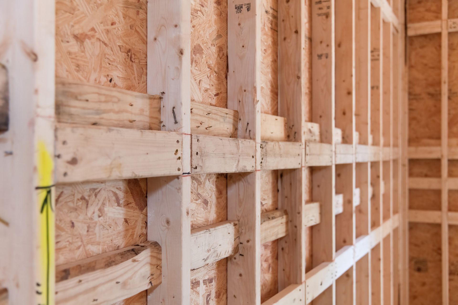 Wooden wall framing inside a construction site, with studs and sheathing boards visible.