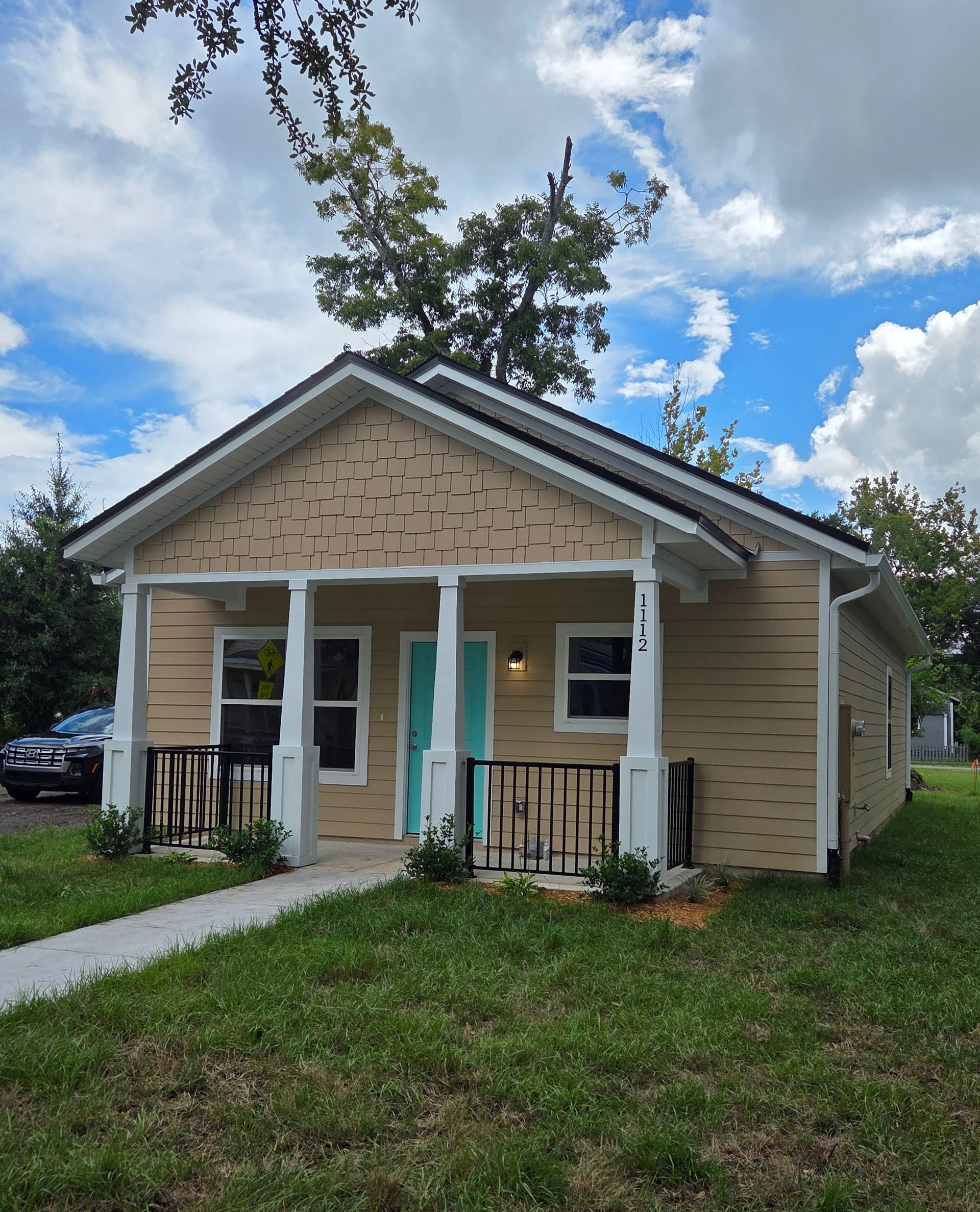 Small beige house with teal front door, white trim, and a grassy yard under a partly cloudy sky