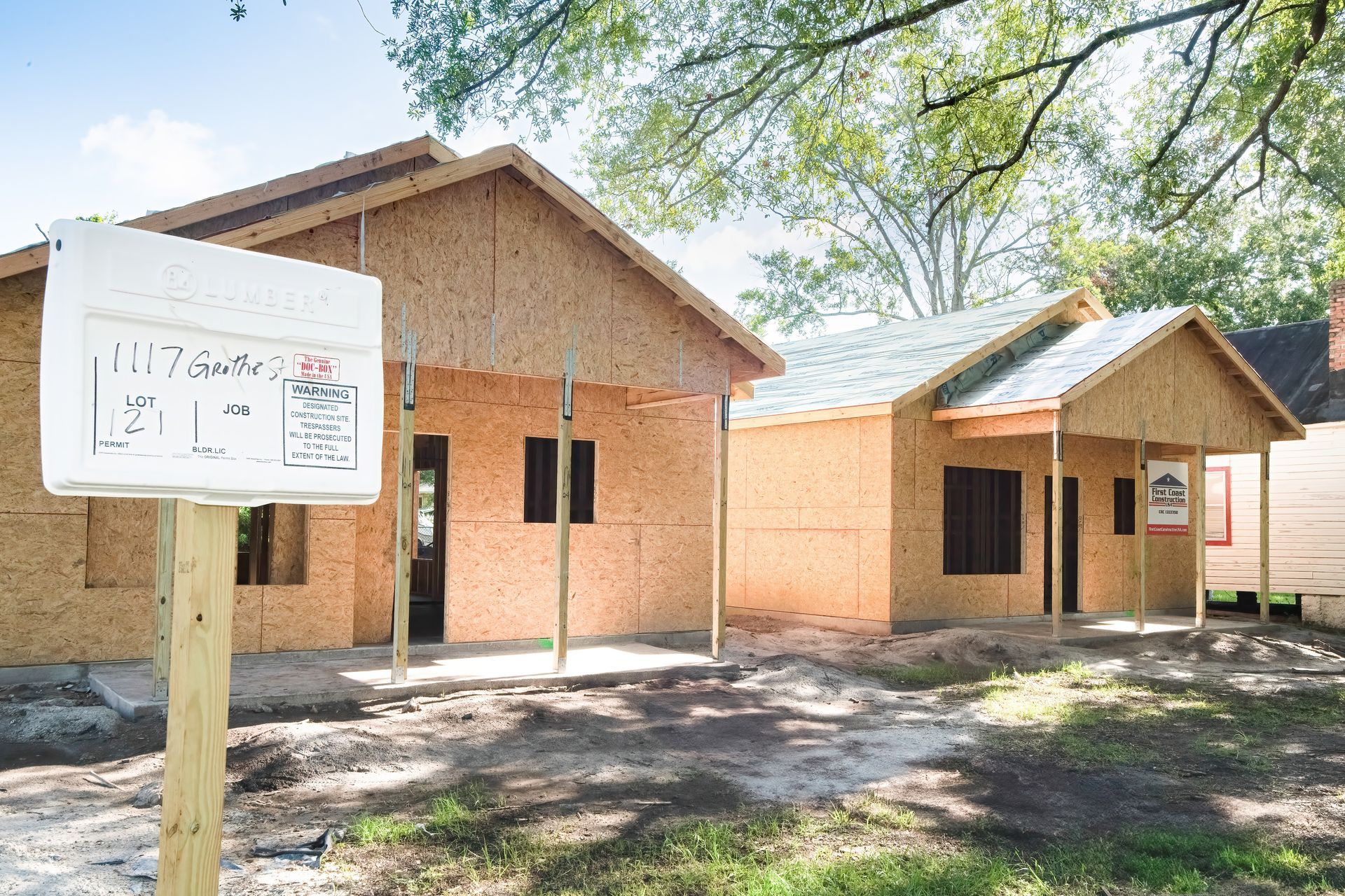 Two small brick buildings with a sign in front, set among trees and dirt ground.