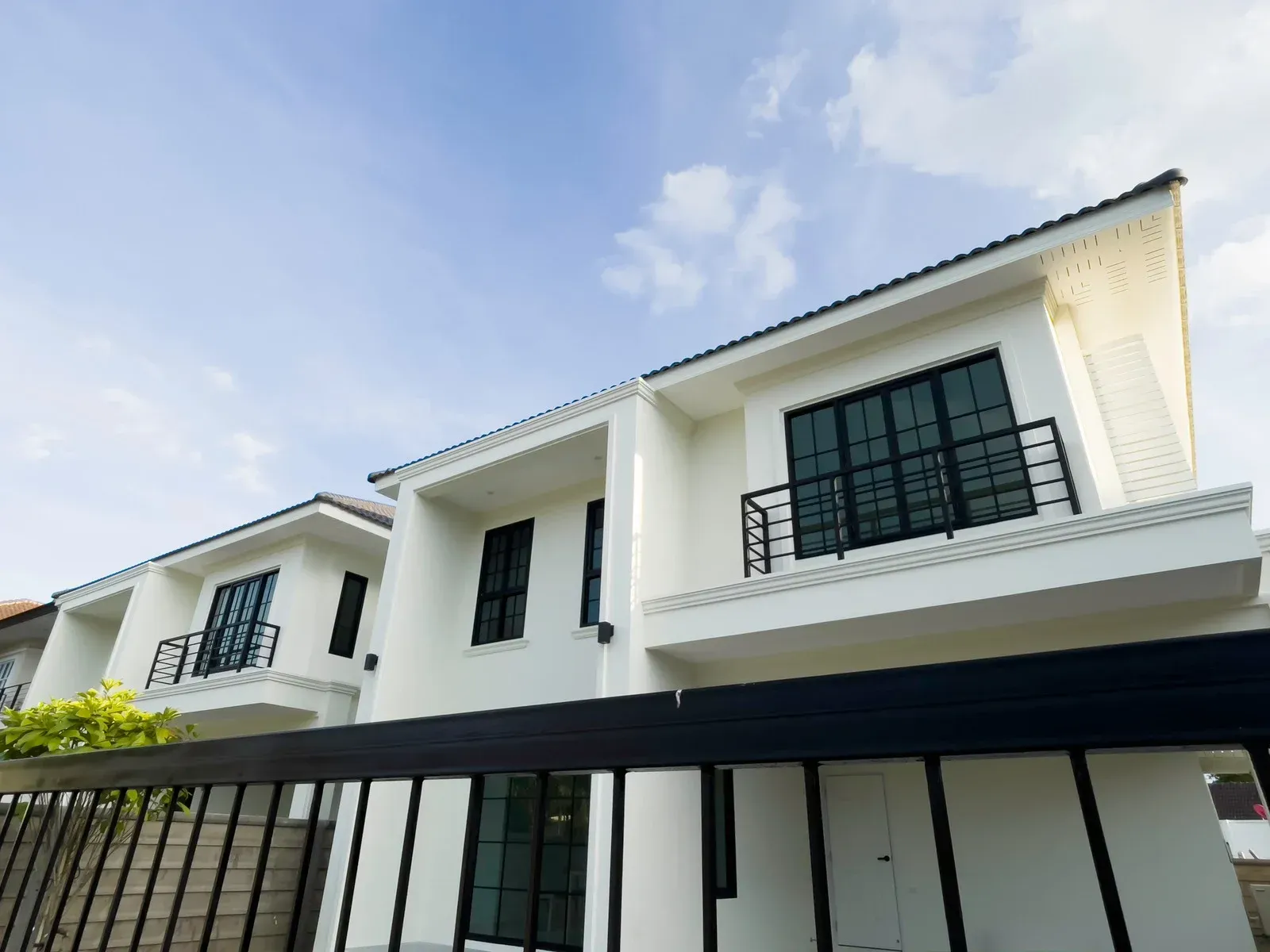 Modern white two-story house with black-framed windows and balconies under a bright blue sky