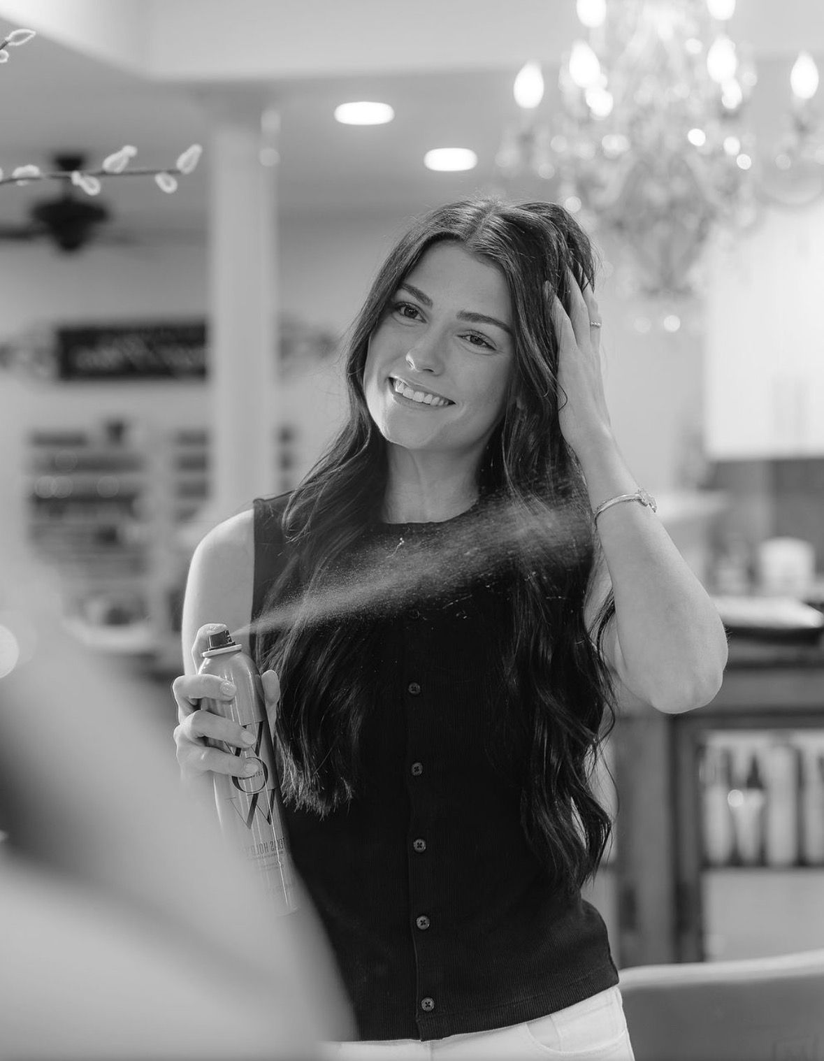 Smiling woman spraying perfume in a store, holding a bottle and touching her hair.
