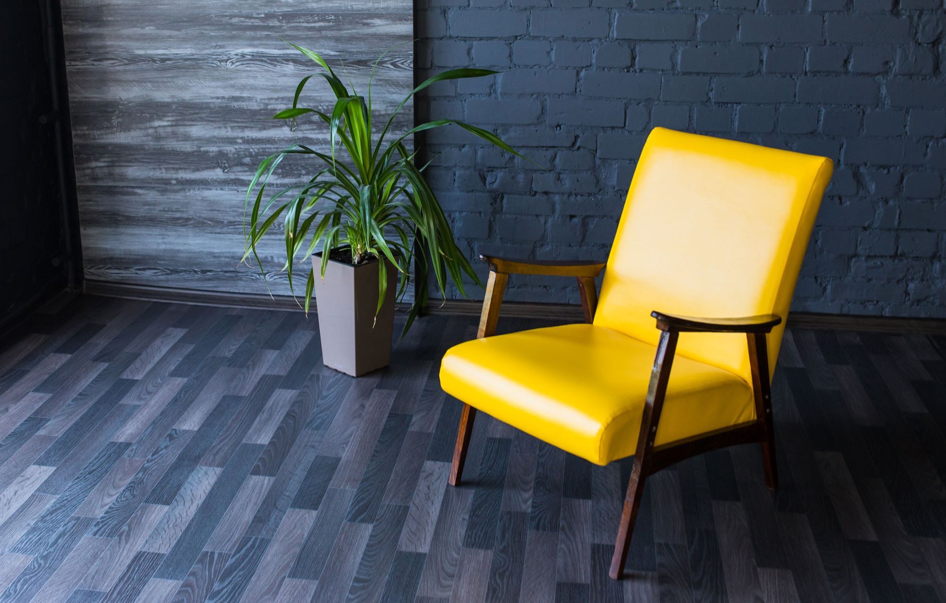Yellow armchair in room with plant and dark walls, wood floor.