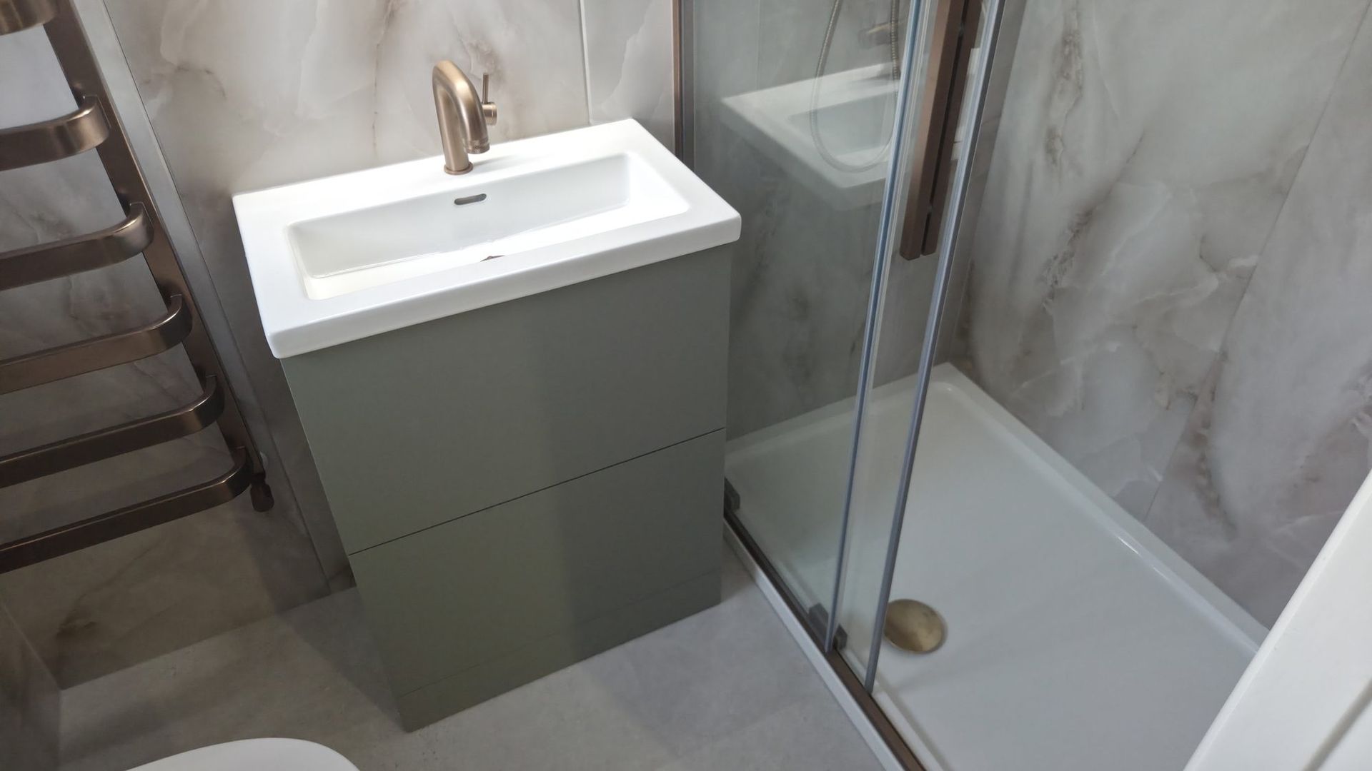 Sage green vanity unit with bronze tap beside a glass shower enclosure