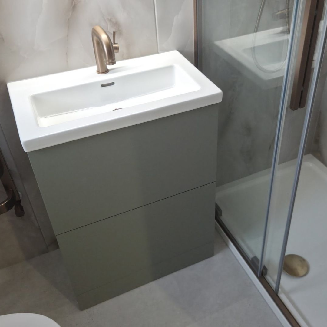 Sage green vanity unit with bronze tap beside a glass shower enclosure