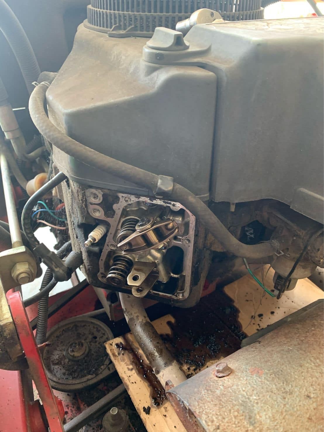 Close-up of a small engine or generator with exposed metal parts, hoses, and a black fuel tank, resting on a workbench.