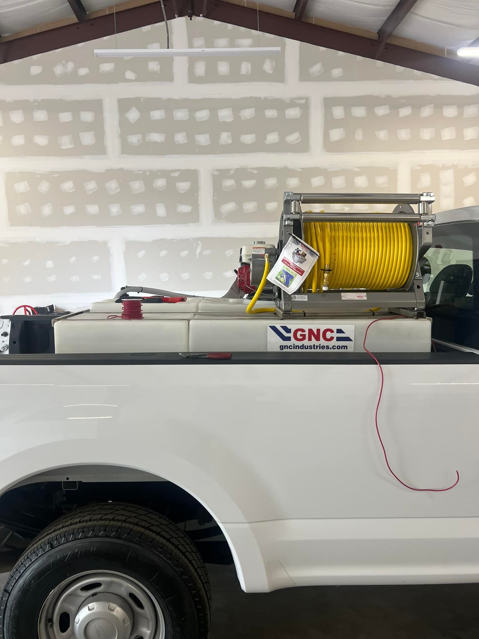 White pickup truck with a yellow hose reel and GNC branding in a garage under construction