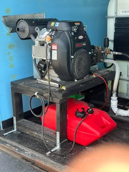 Industrial machine on a metal frame with red tank and black motor in a workshop, connected to pipes and hoses