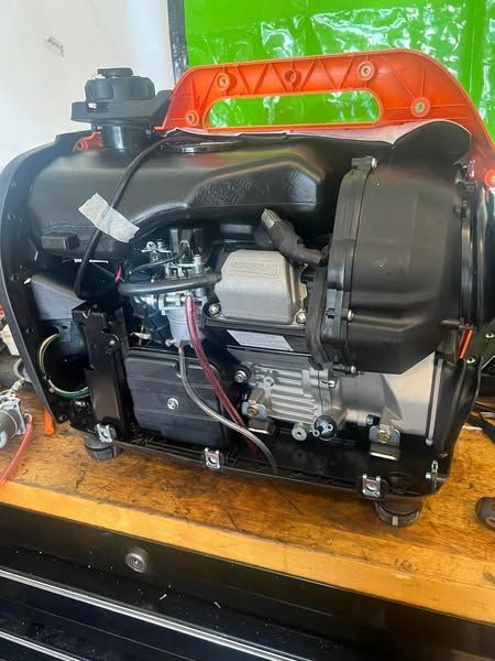 Black industrial machine or engine assembly with orange handle on a wooden table