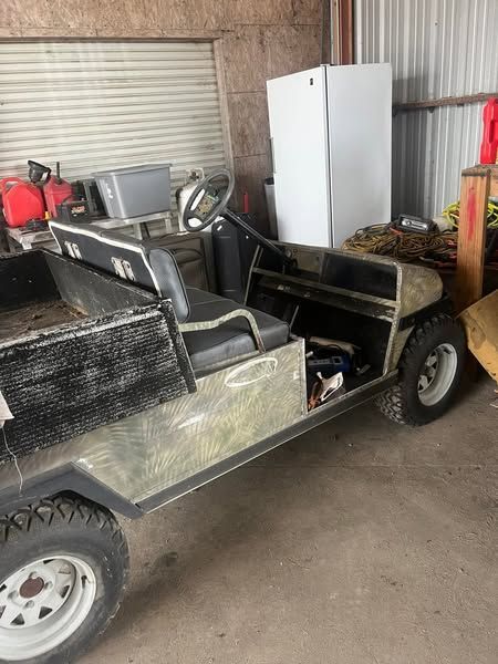 Small open utility cart in a garage, with black seats, a white cabinet, and tools in the back.