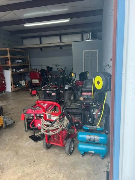 Garage filled with lawn equipment, generators, and tools, with a red pressure washer in front.