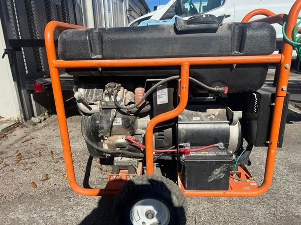 Orange-framed portable generator on a wheeled cart outdoors beside a corrugated metal wall