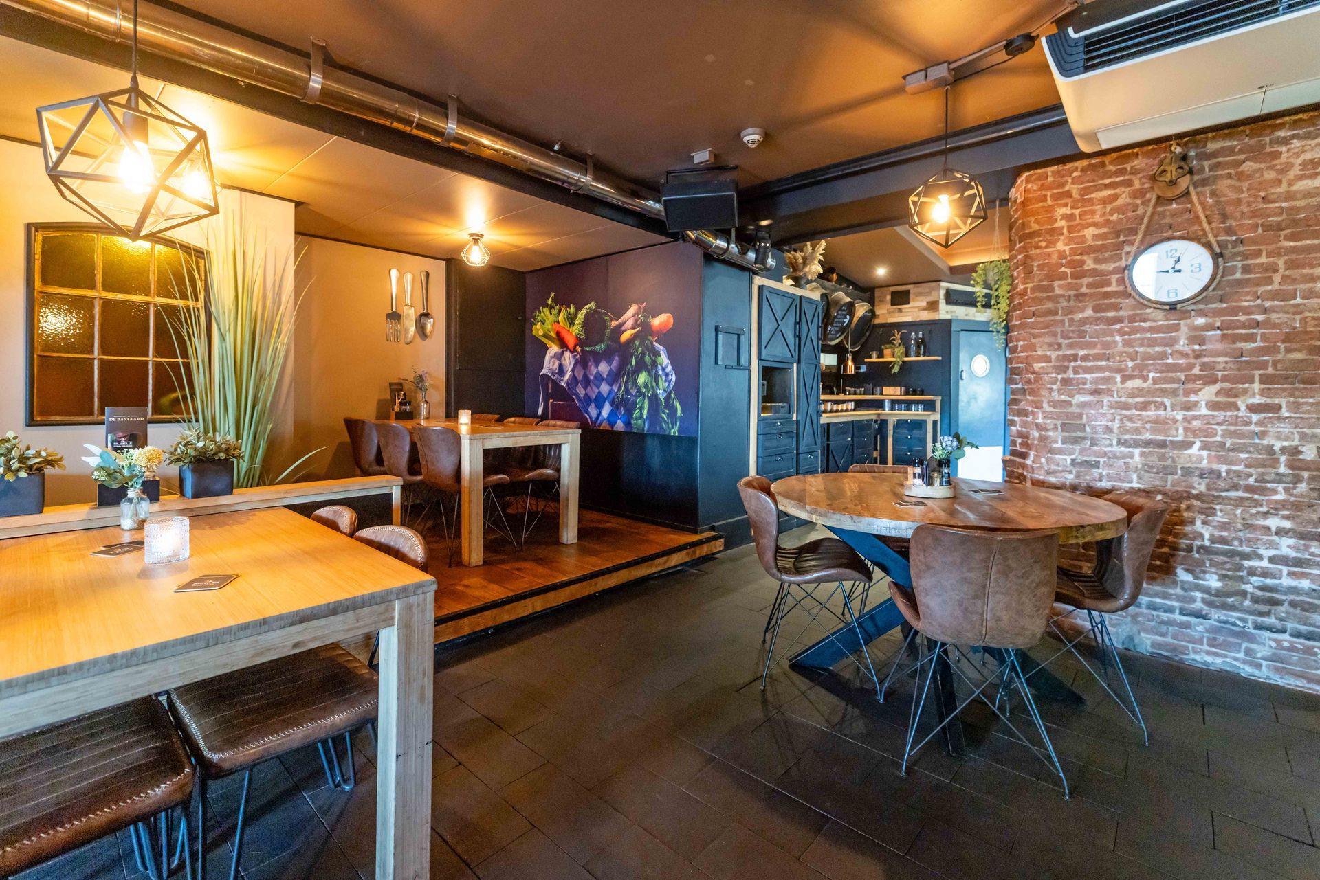 Een sfeervol restaurantinterieur met houten tafels, een bakstenen muur en hanglampen in een knusse eetruimte.