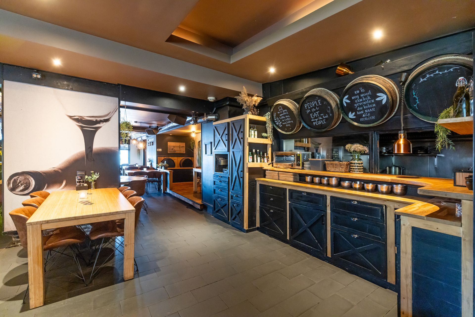 Warm en modern barinterieur met houten tafel, blauwe kasten en grote ronde wandklokken.