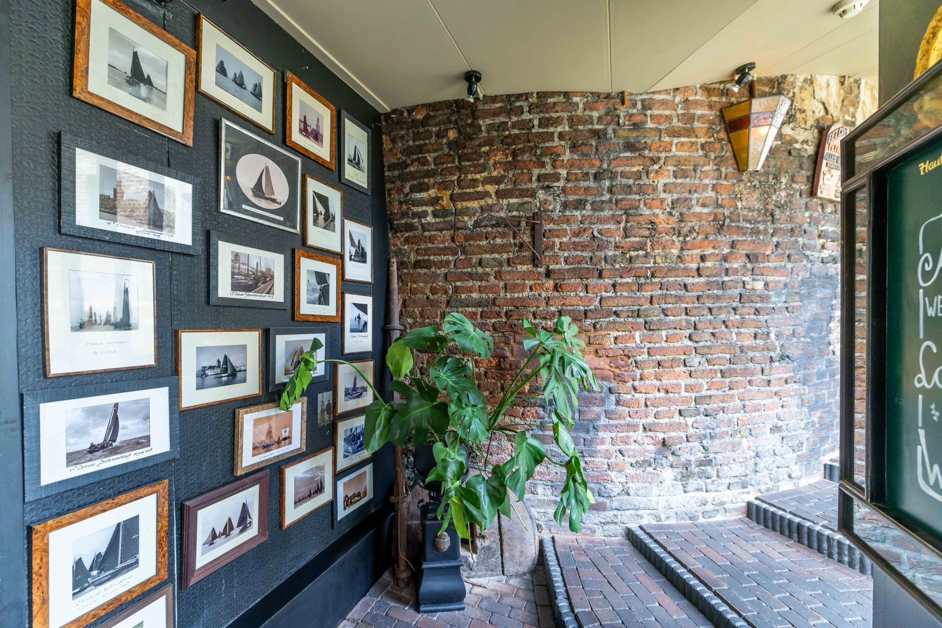 Een hal in galerijstijl met ingelijste foto's aan een donkere muur, oude stadsmuur doorloop naar café/restaurant