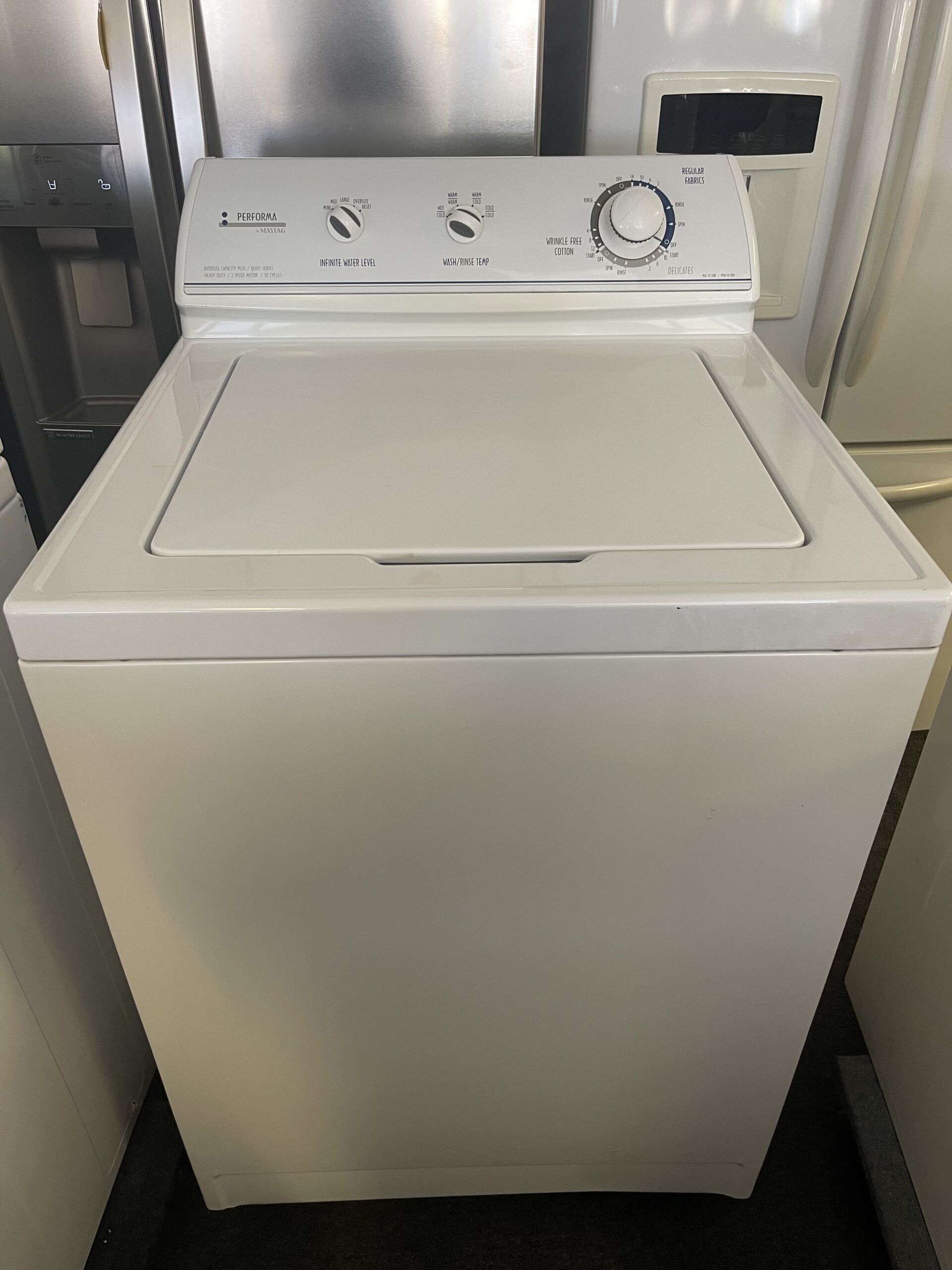 A white washing machine is sitting on the floor next to a refrigerator.