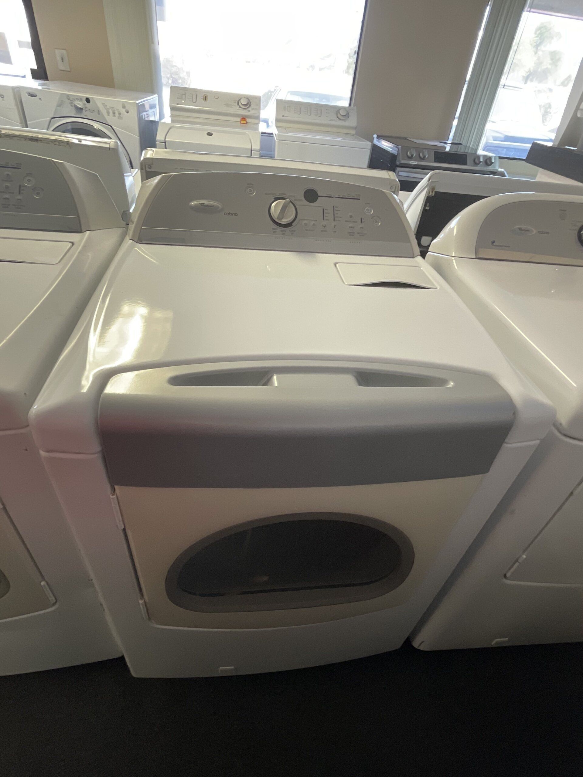 A row of white washers and dryers are lined up in a store.
