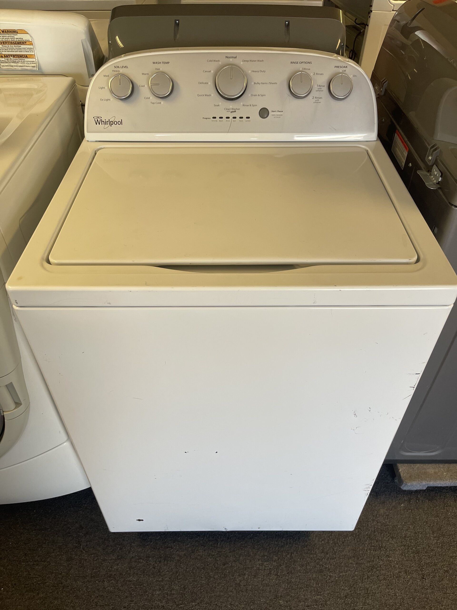 A white washing machine is sitting on top of a carpeted floor.