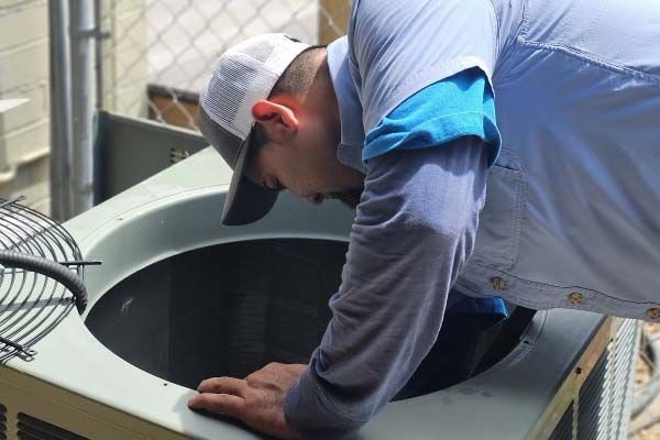 Technician leaning over an open HVAC unit, inspecting the interior during maintenance.