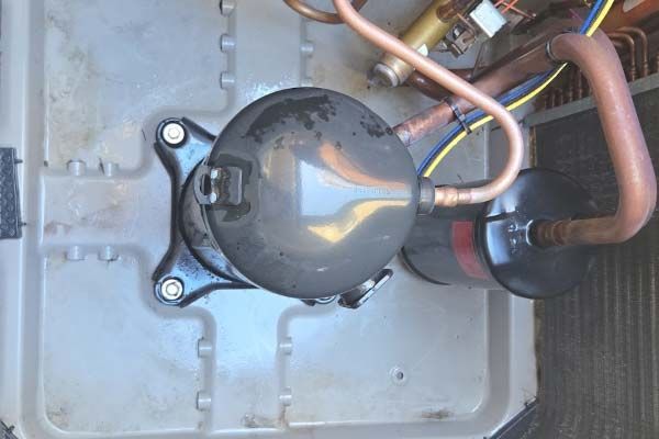 Close-up of a black refrigeration compressor with copper pipes in a metal compartment