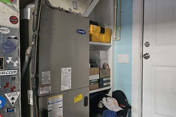 Utility closet with furnace, shelves, and a white door; clothes and bags are piled on the floor.