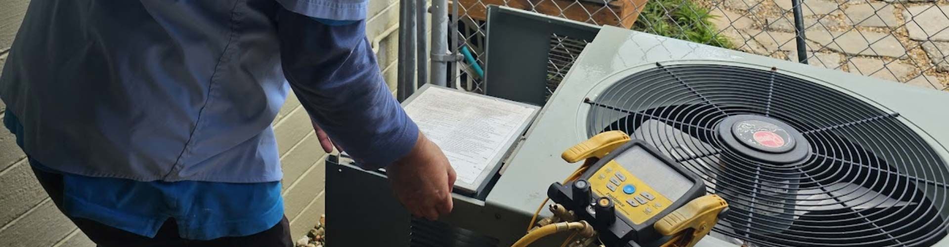 Worker inspecting outdoor HVAC unit with open panel and visible fan.