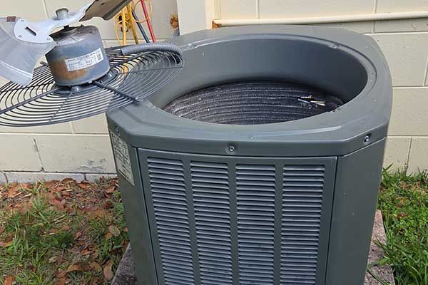 Outdoor air conditioner unit beside a wall, with a fan and leaves around it