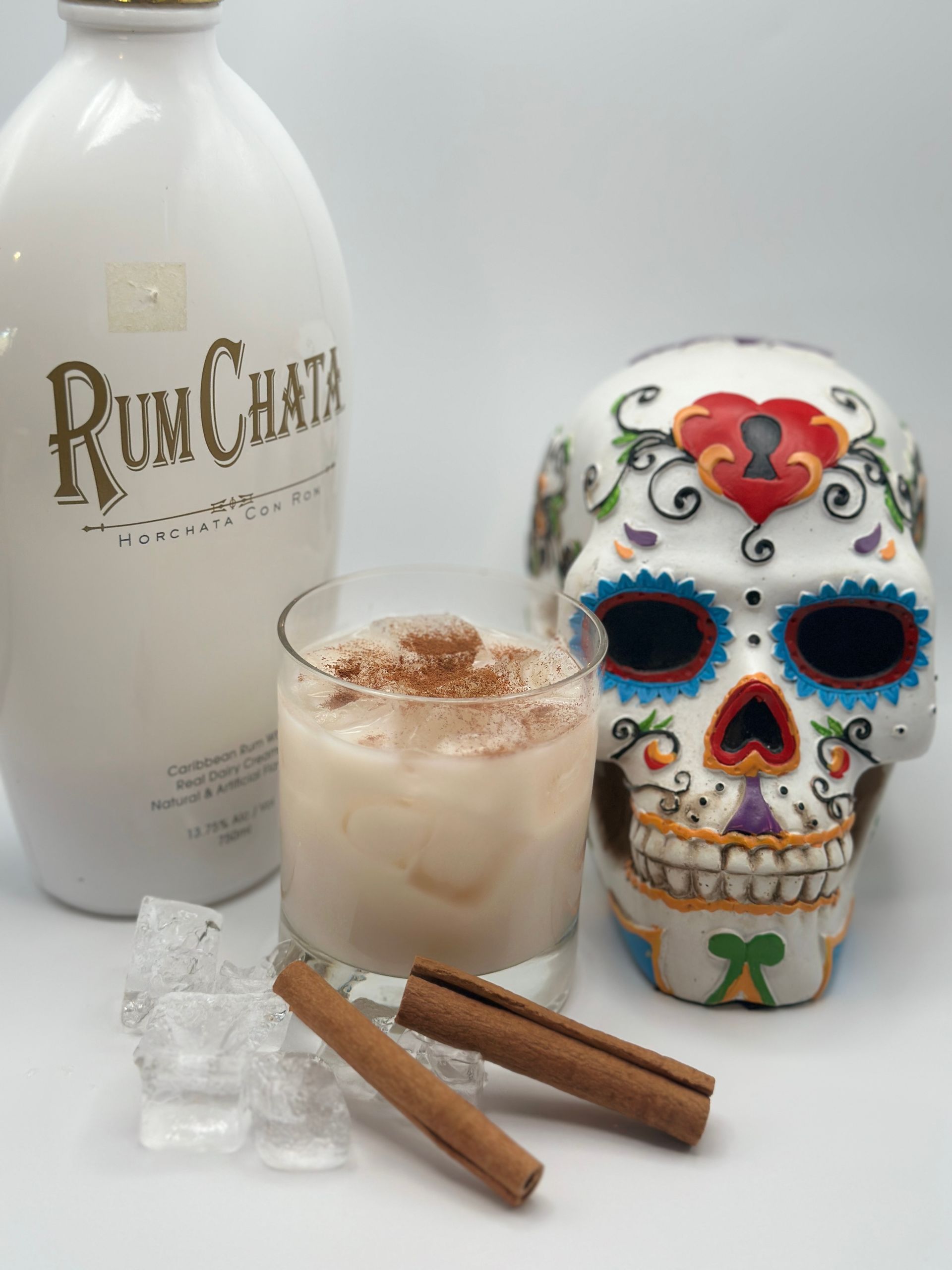 RumChata cocktail in a glass with a skull, cinnamon sticks, and ice. The RumChata bottle is visible.