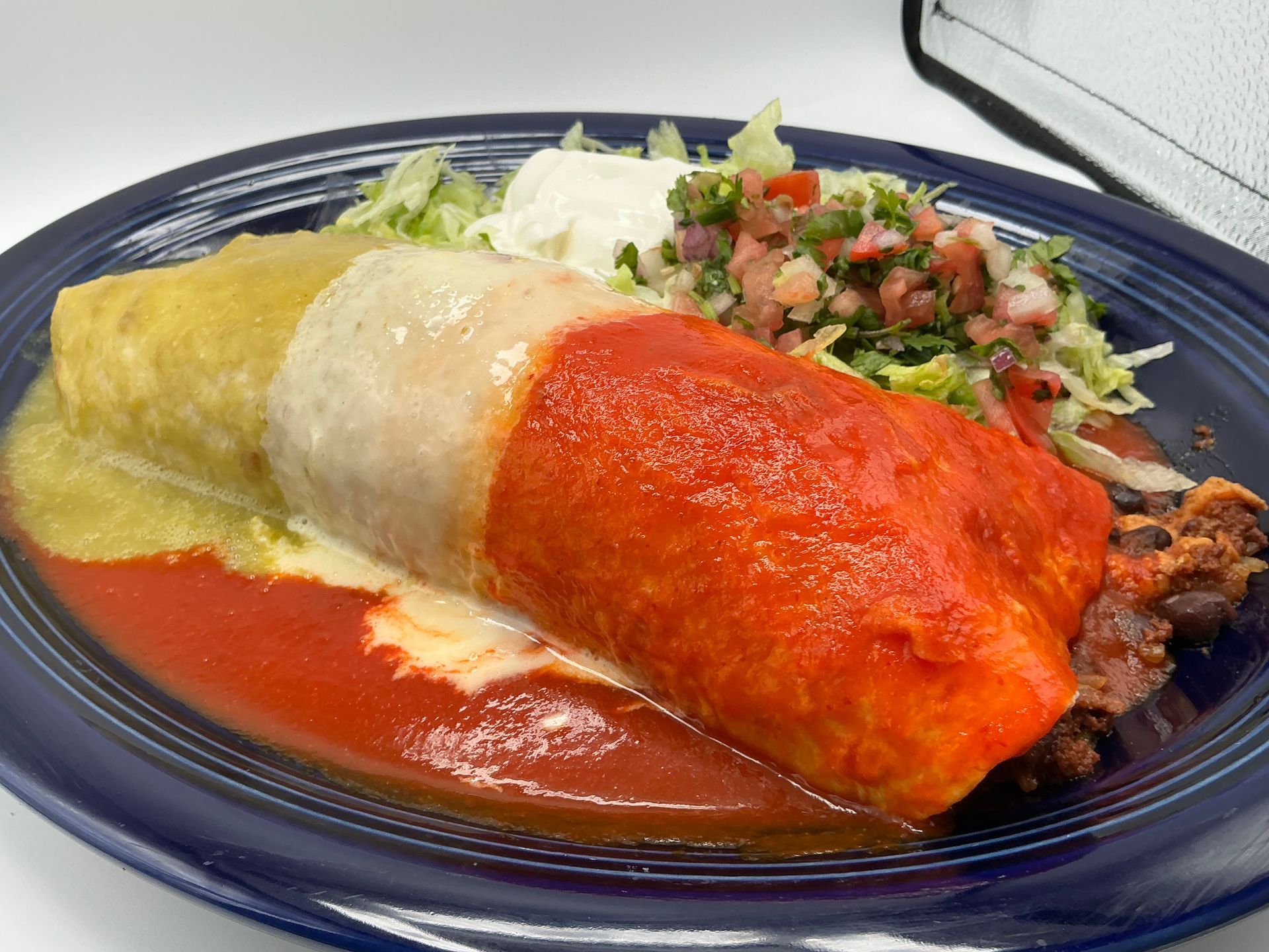 Burrito covered in red and green sauces, with toppings of sour cream, pico de gallo, and shredded lettuce.