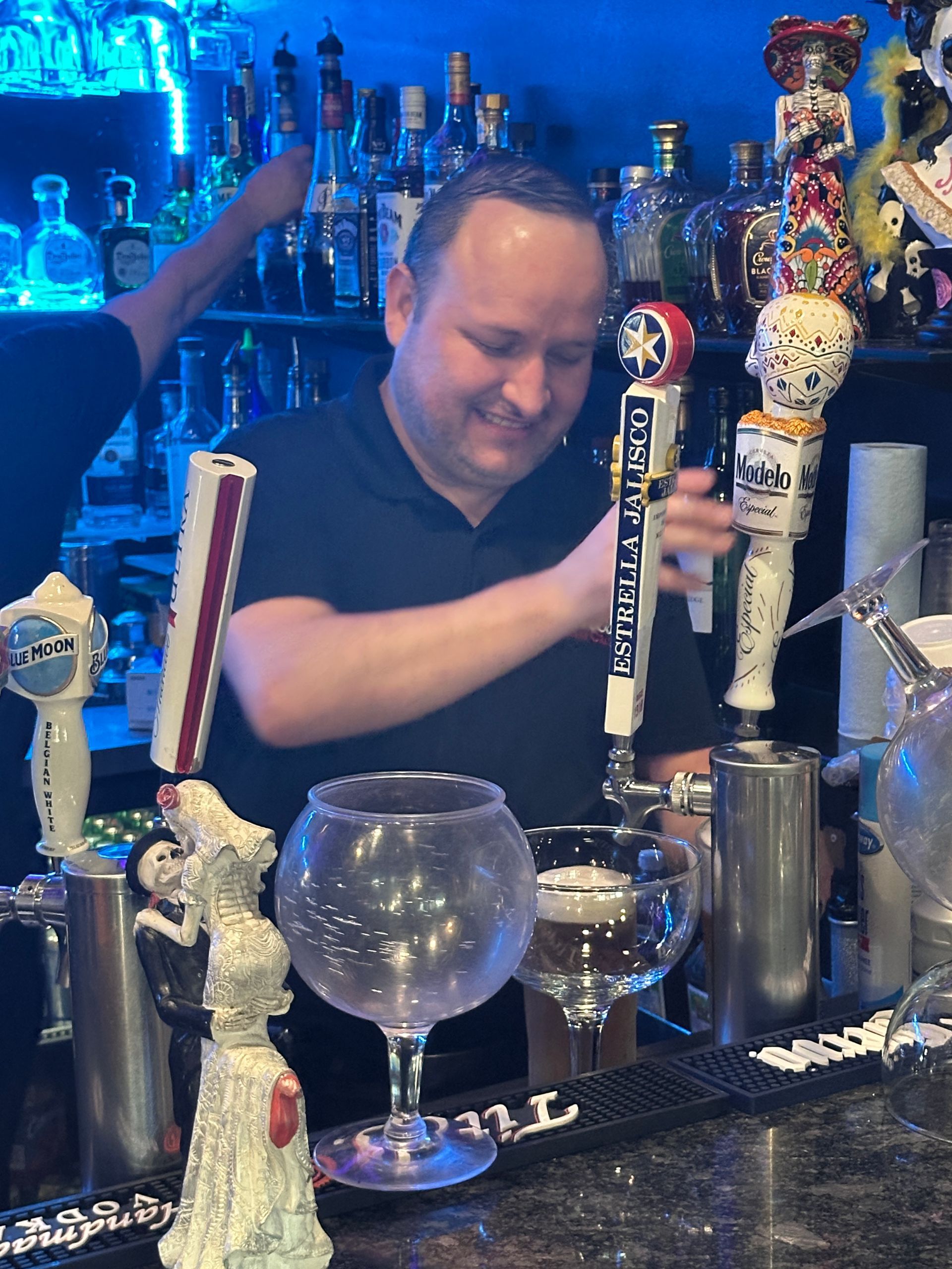 Bartender pouring a drink at a bar; bottles in the background.